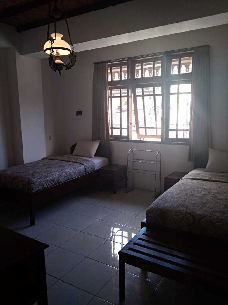 A room with two beds, a hanging light fixture, a window with curtains, and a tiled floor.
