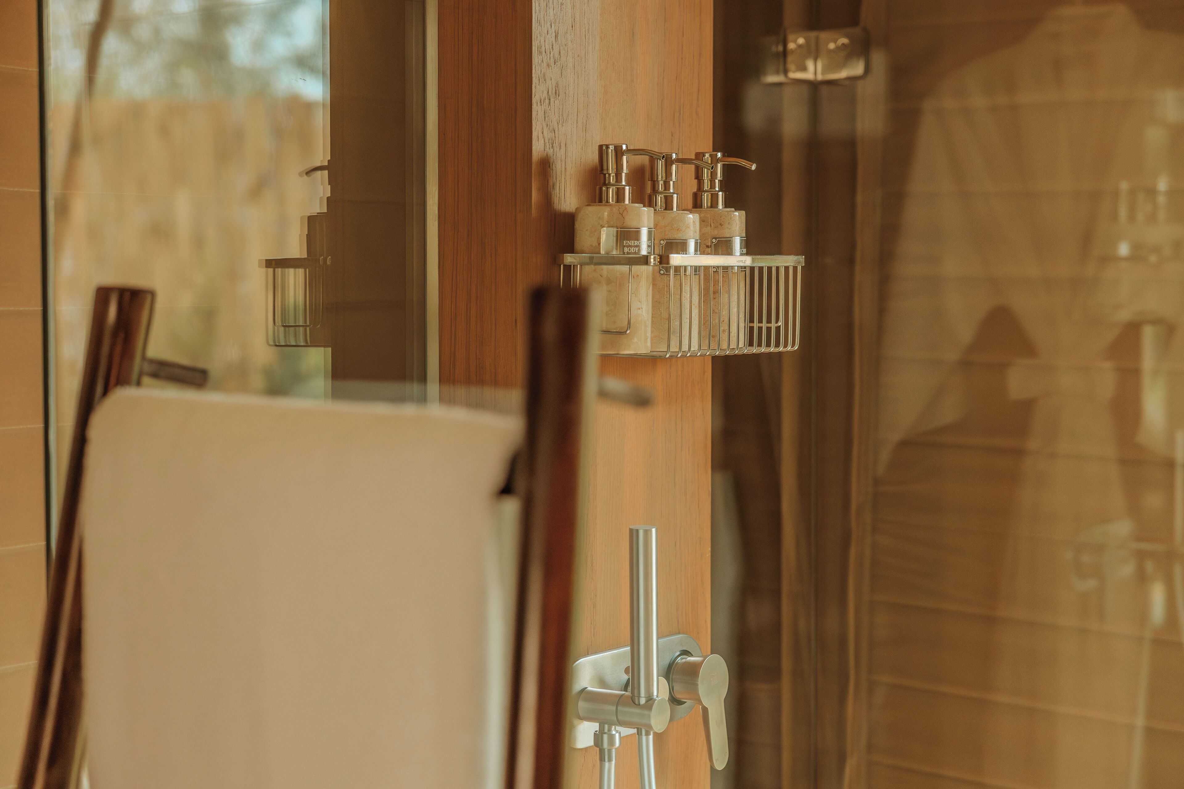A bathroom with a glass shower enclosure, a wooden door, and a towel rack with toiletries.