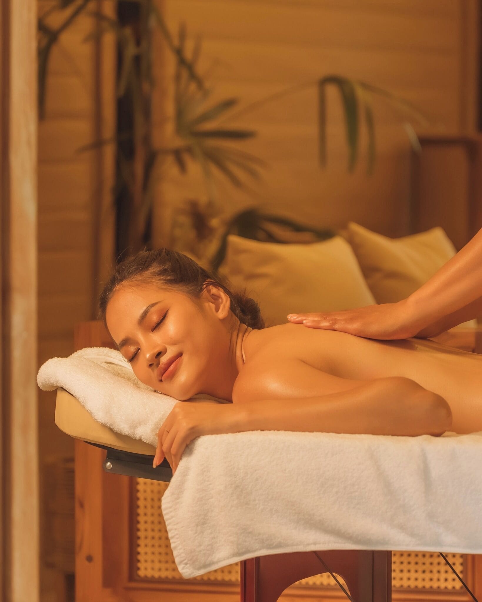 A person receiving a massage in a room with wooden walls and a plant in the background.