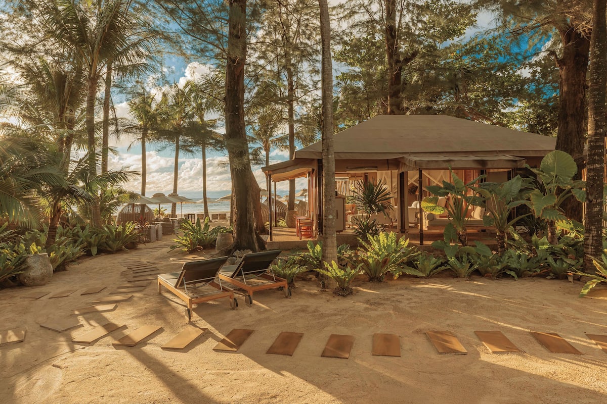 Ett semesterhotell vid stranden med ett takförsett sittområde, solstolar och utsikt över havet.