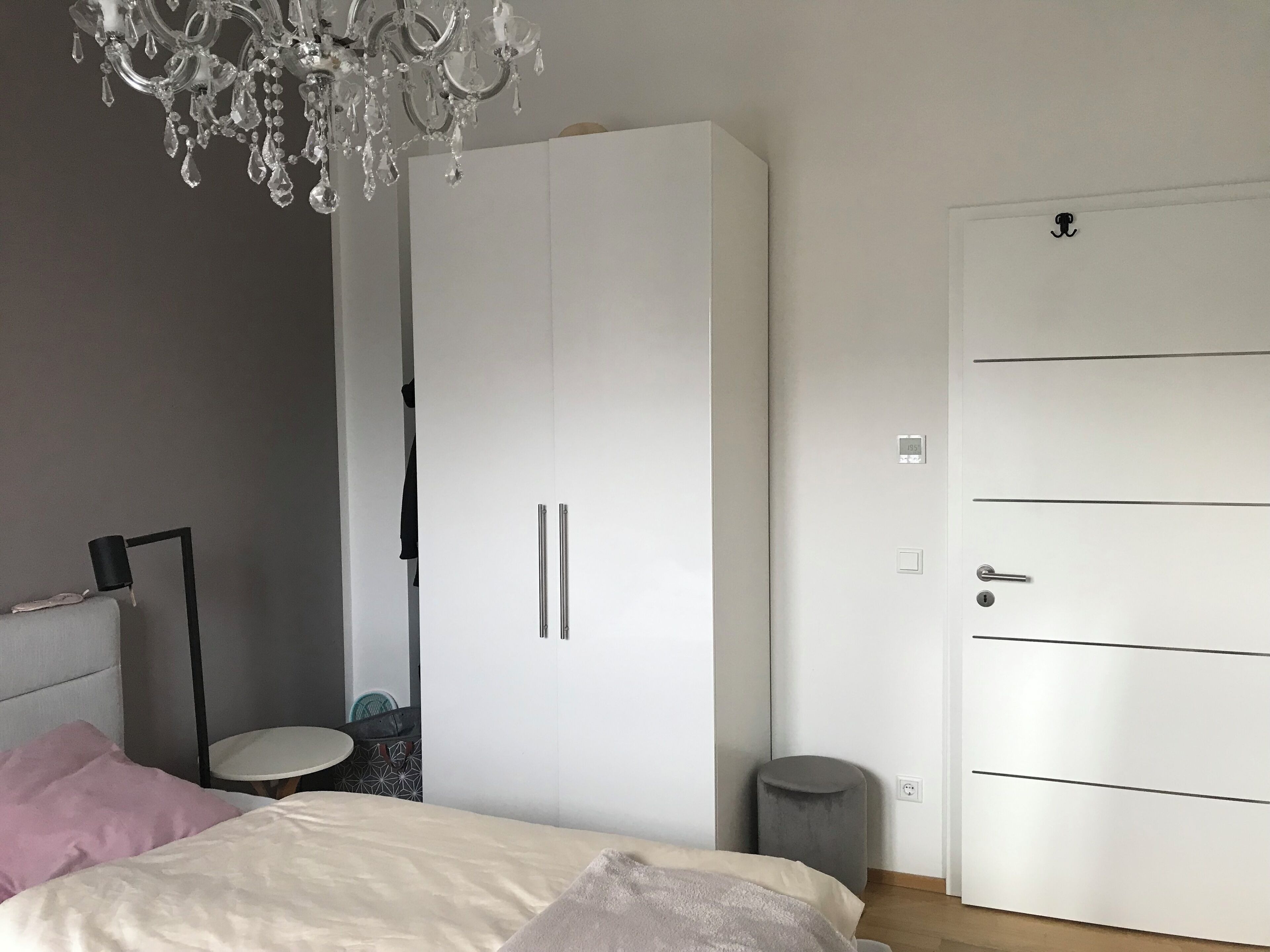 Une chambre à coucher avec un lit, une armoire, une porte, une poubelle et un lustre.