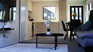 Una sala de estar moderna con una televisión de pantalla plana, una mesa redonda de centro, un sofá y un comedor con una silla y una mesa.