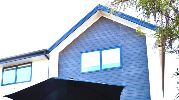 Una casa moderna con un patio que cuenta con una mesa, sillas, una sombrilla y césped.