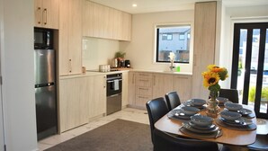 Una cocina moderna con armarios de madera clara, electrodomésticos de acero inoxidable y una zona de comedor con una mesa dispuesta para cuatro.