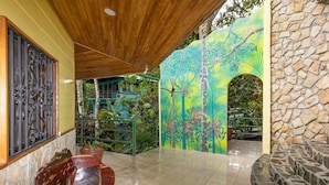Un’area esterna coperta con pareti in pietra, un murale raffigurante una scena tropicale e un’area relax con panche in legno.