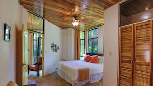 Una camera da letto con un letto, una sedia, un ventilatore a soffitto e persiane di legno.