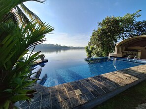 Una piscina infinita con vistas despejadas a un lago tranquilo, rodeada de exuberante vegetación y una terraza de piedra.