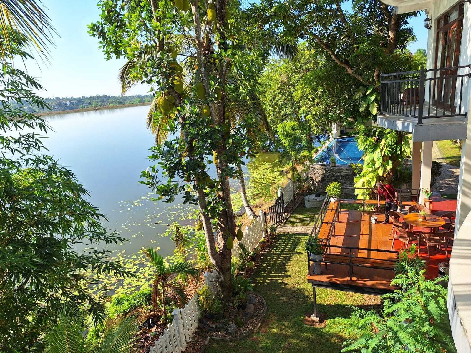 Terraza con mobiliario exterior con vistas a un lago, rodeada de abundante vegetación y un muro de piedra.