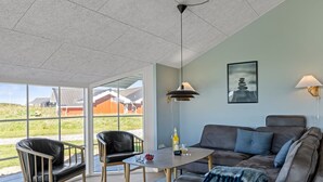Un salon moderne comprenant un canapé, des fauteuils, une table et une grande fenêtre donnant sur des maisons.