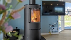 Un salon moderne doté d’un poêle à bois, d’un téléviseur à écran plat fixé au mur et d’une fenêtre donnant sur l’extérieur.