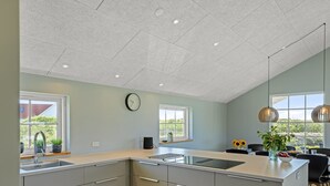 Une cuisine moderne dotée d’un grand îlot central, d’appareils électroménagers intégrés et bénéficiant d’un éclairage naturel abondant grâce à de grandes fenêtres.