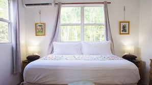 Ein ordentlich bezogenes Bett mit Blumendekoration, zwei Nachttischlampen und ein Fenster mit Vorhängen.