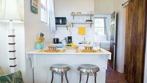 Eine kleine Küche mit weißer Arbeitsplatte, zwei Hocker, einer Mikrowelle und einer Kaffeemaschine.
