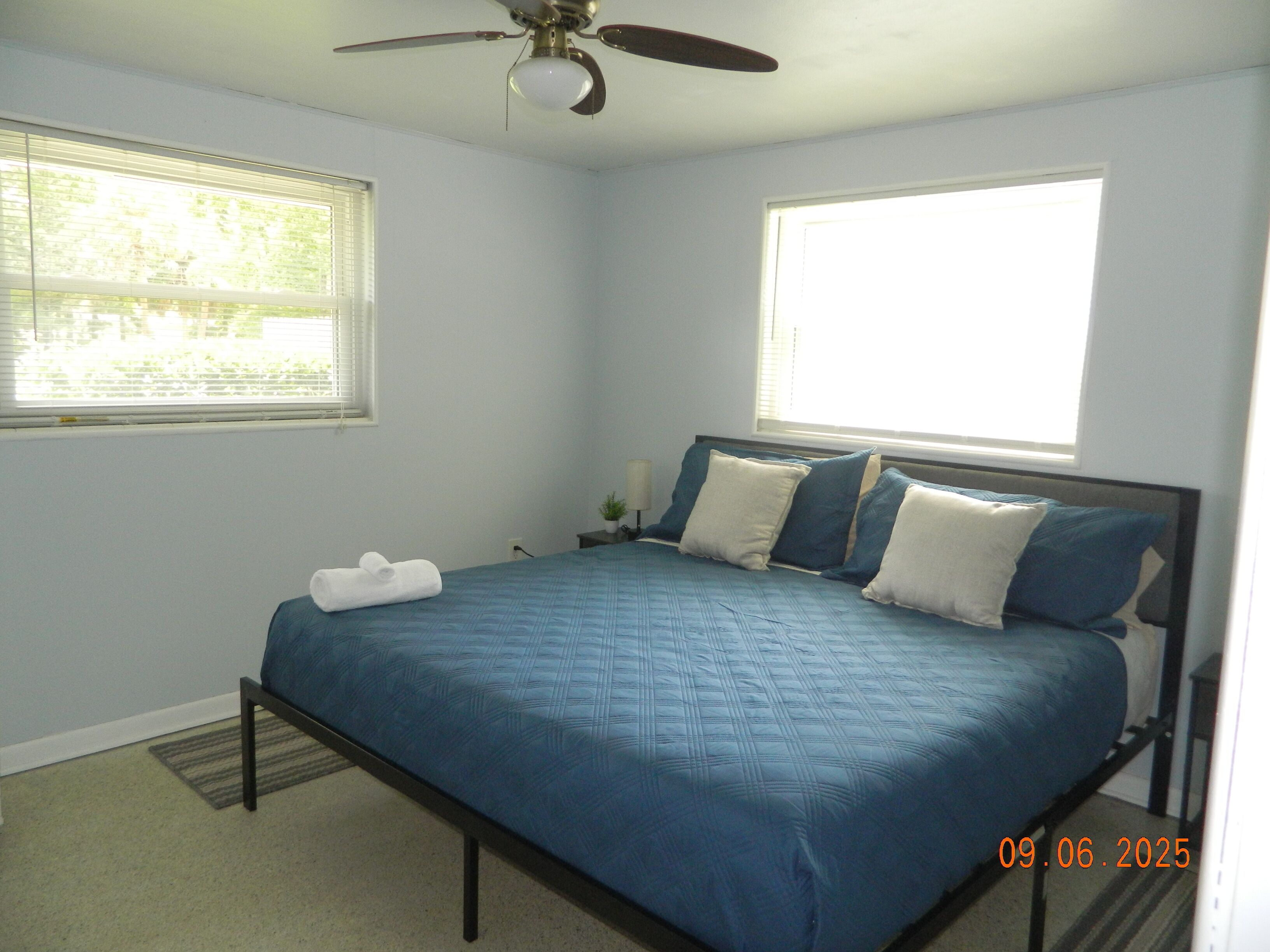 A bedroom with a bed, two windows, a ceiling fan, and a nightstand.