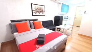 A hotel room with a bed, a desk, a chair, a TV, and a kitchen area.