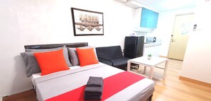 Quarto de hotel com cama, escrivaninha, cadeira, televisão e cozinha.