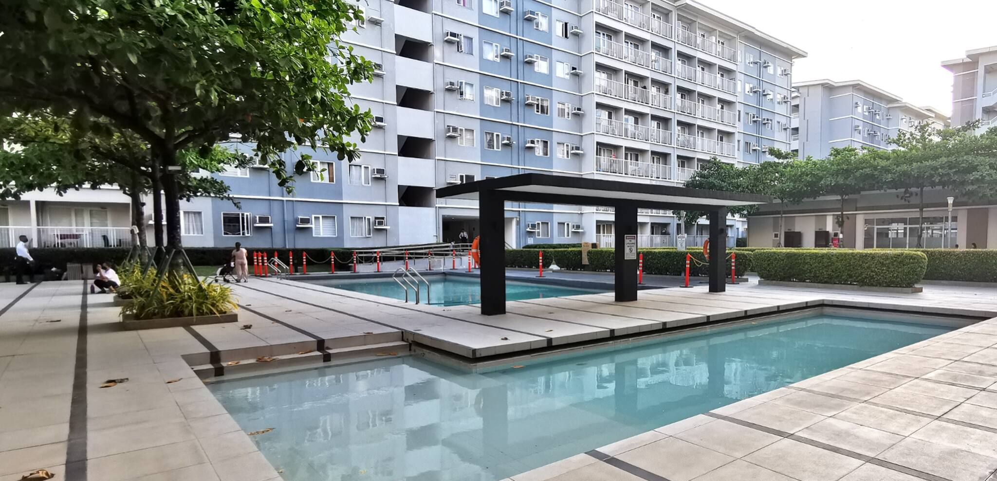 A swimming pool area with a covered seating area, surrounded by a modern apartment building.