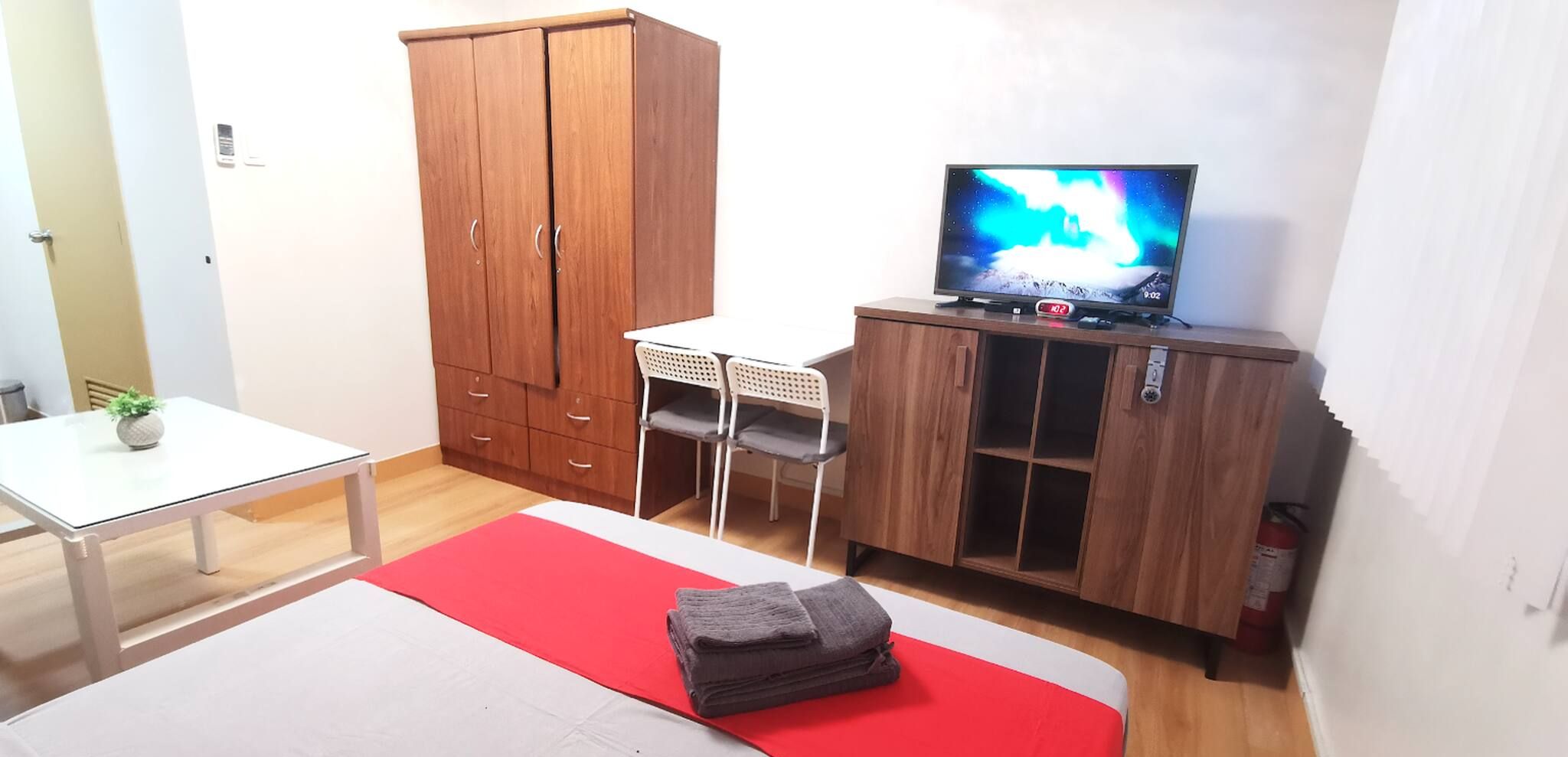 Un dormitorio con cama, televisor, armario y una mesita.