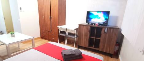 Un dormitorio con cama, televisor, armario y una mesita.