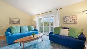 A living room with two blue sofas, a wooden coffee table, and a large window with a view of greenery. - Aqua Oasis - Beach Days & Holiday Nights! (St. Augustine Beach)