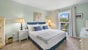 A bedroom with a bed, two bedside tables with lamps, a dresser, and a window with curtains. - Aqua Oasis - Beach Days & Holiday Nights! (St. Augustine Beach)