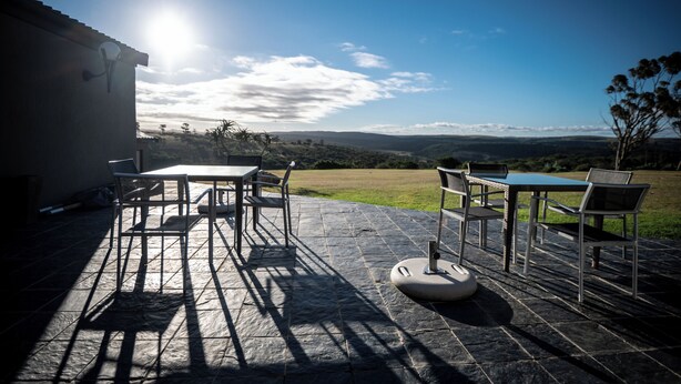 Um pátio externo com mesa e cadeiras, piso de pedra e vista para o campo.