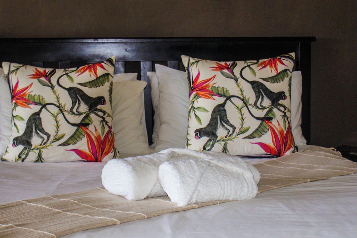 A neatly made bed with two pillows featuring a monkey and floral pattern, a white towel, and a wooden headboard.