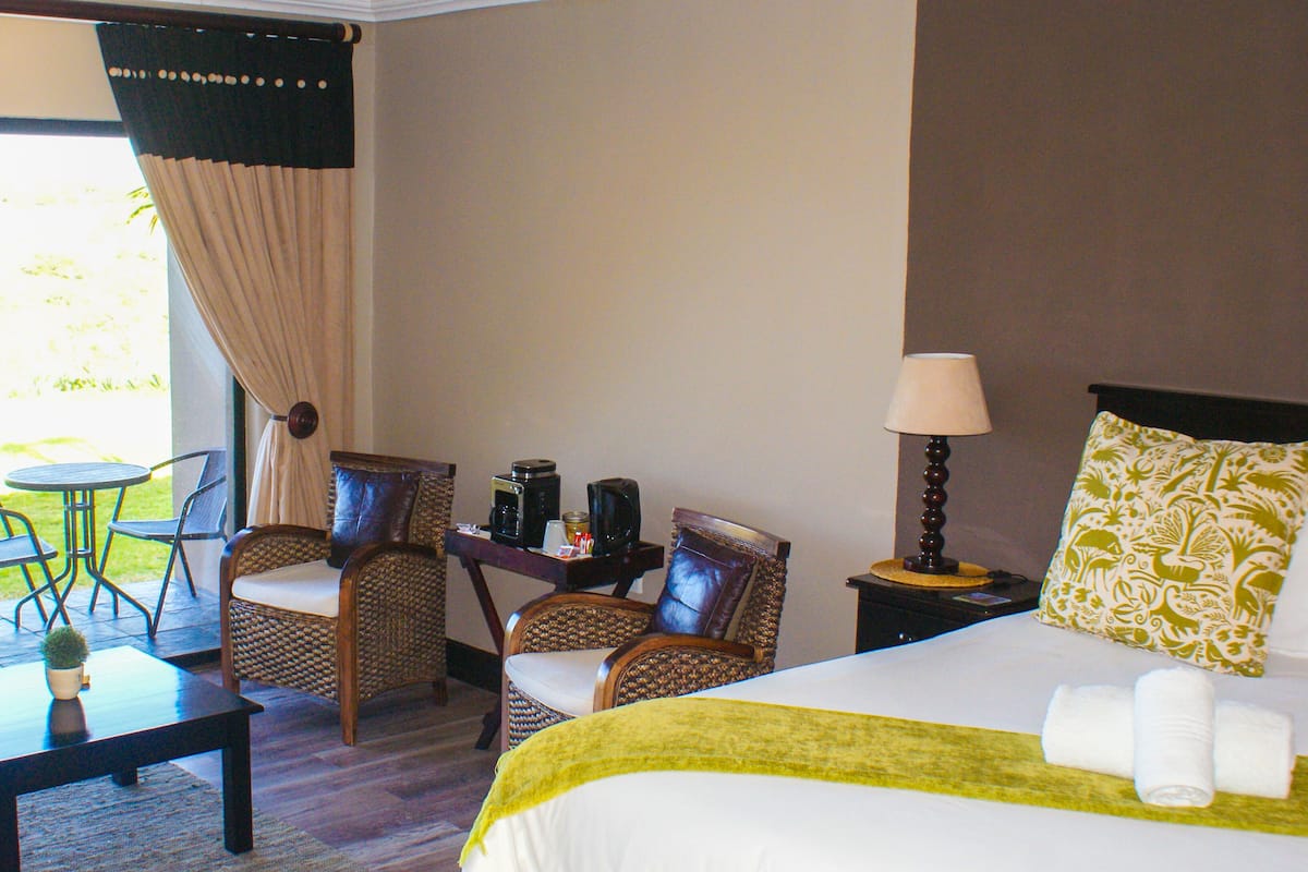A hotel room with a bed, two chairs, a small table, a lamp, and a coffee maker.