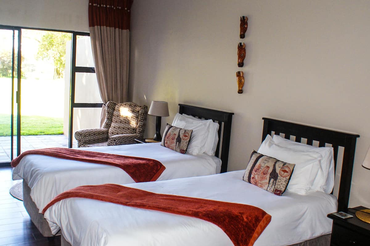 A hotel room with two beds, a chair, a lamp, and a view of the outdoors.