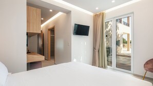 A modern hotel room with a bed, a TV mounted on the wall, a sliding glass door to the outside, and a wooden cabinet. - Heated pool, outdoor playground, convenient location close to the beach and town (Rethymno)