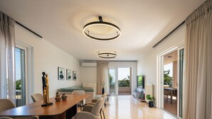 A modern living room with a dining area, large windows, and a view of the outdoors. - Heated pool, outdoor playground, convenient location close to the beach and town (Rethymno)