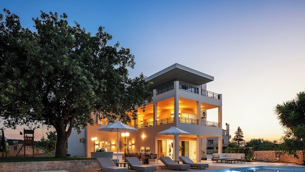 A modern two-story house with a swimming pool, outdoor seating, and a well-lit balcony. - Heated pool, outdoor playground, convenient location close to the beach and town (Rethymno)