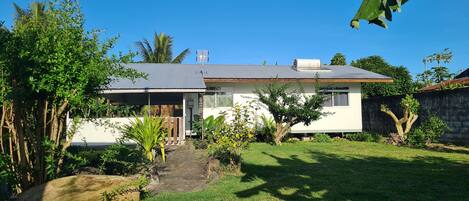 A house with a sloped roof, a front porch, and a small garden with various plants and a pathway leading to the entrance.