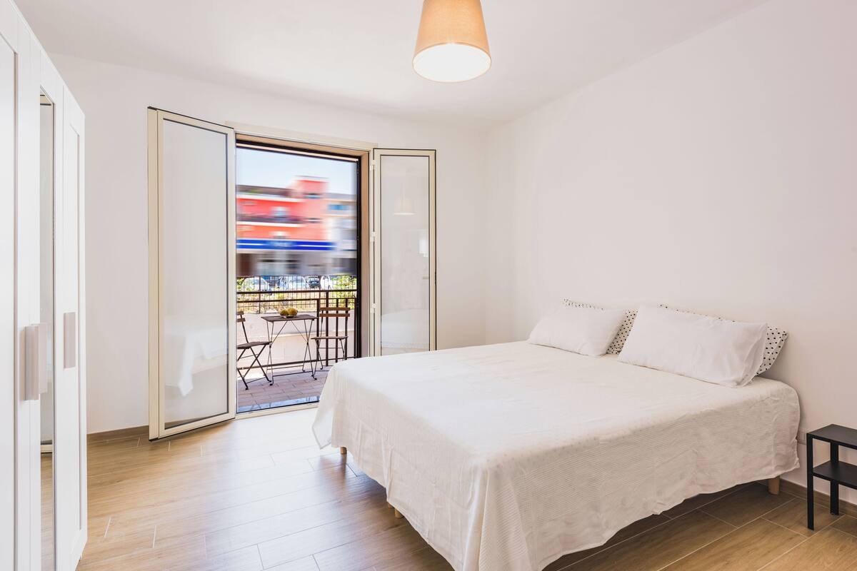 Ein Schlafzimmer mit einem großen Bett, einer Schiebetür zu einem Außenbereich und einer Deckenleuchte.