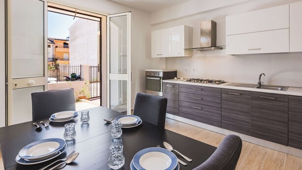 A modern kitchen with dark cabinets, a gas stove, and a sink. There is a dining area with a table set for four, including plates, glasses, and cutlery. - Casa Lilium a Floridia by Wonderful Italy (Floridia)