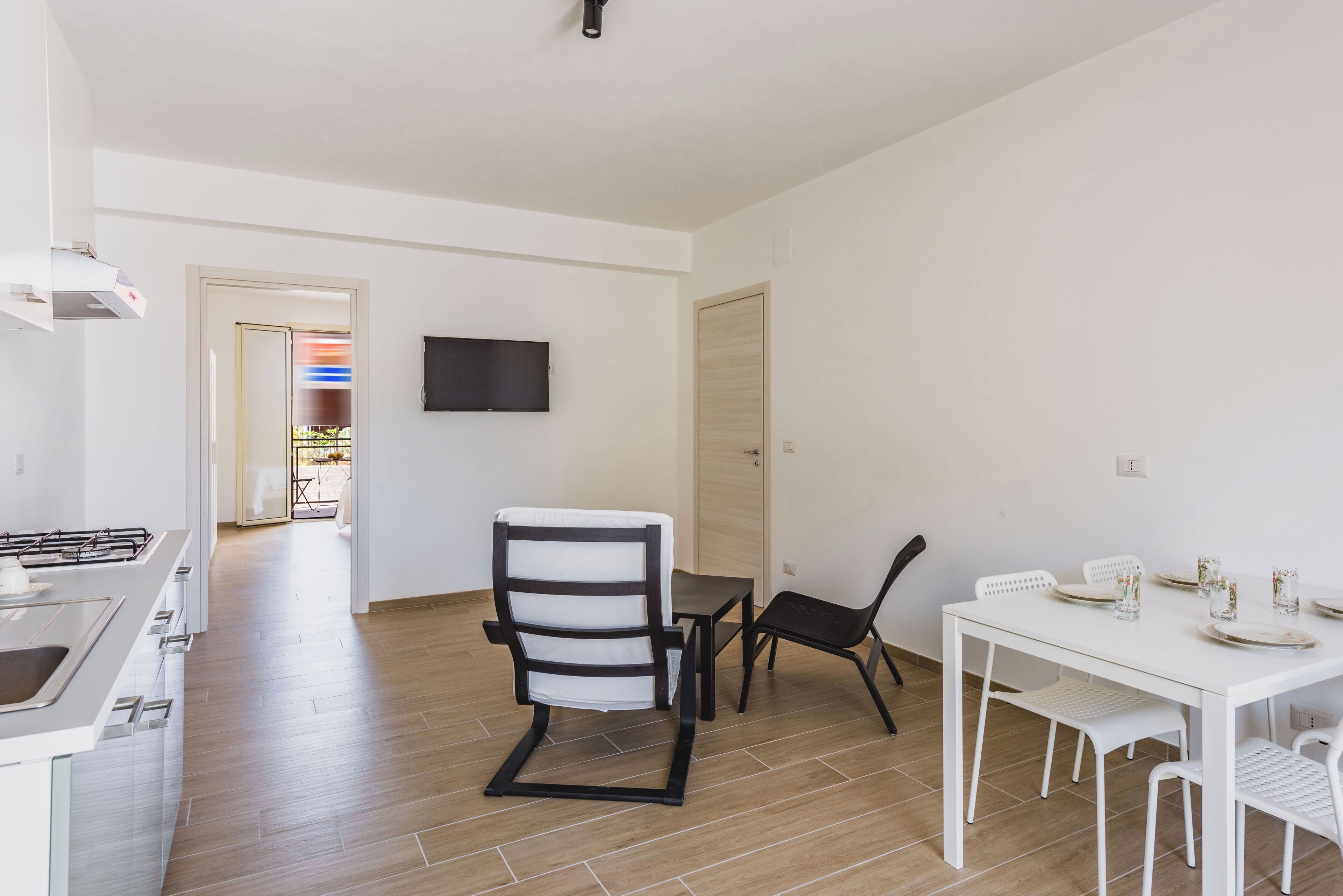 A modern kitchen with a built-in stove, a dining area with a white table and chairs, and a flat-screen TV mounted on the wall.