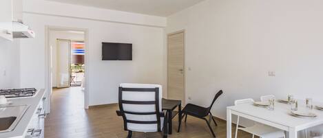 A modern kitchen with a built-in stove, a dining area with a white table and chairs, and a flat-screen TV mounted on the wall.