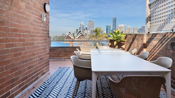 Eine Terrasse mit weißem Tisch und Korbstühlen mit Blick auf eine Stadtlandschaft und markante Gebäude.