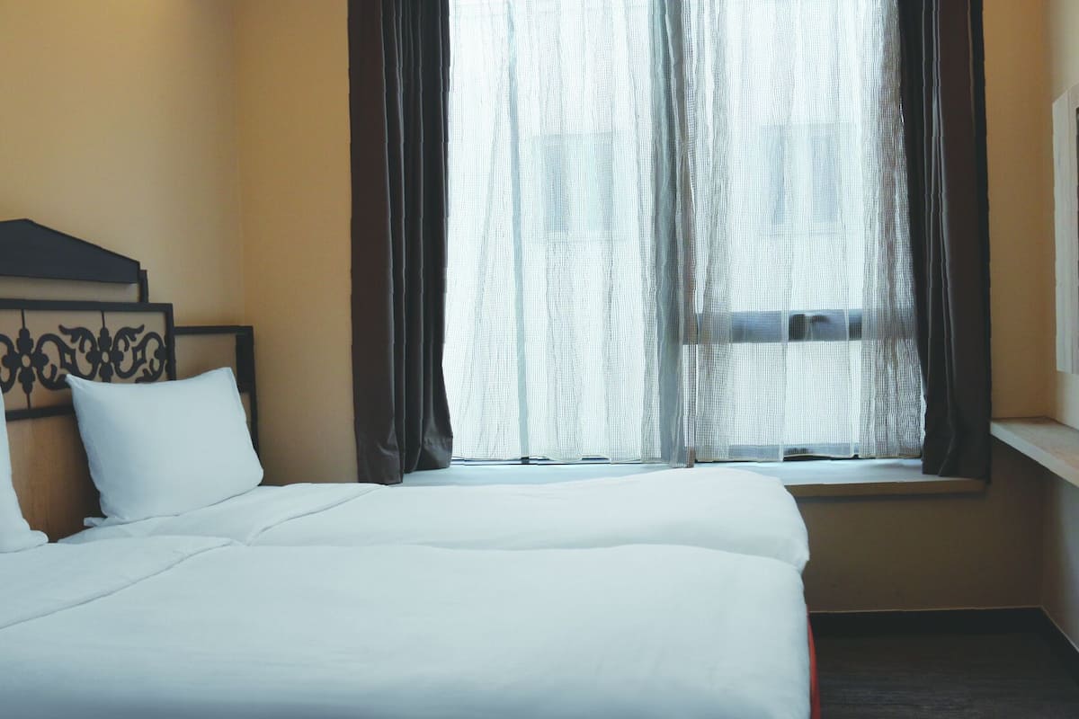 Une chambre d’hôtel avec un grand lit, une fenêtre avec des rideaux légers et une tête de lit ornée d’un motif décoratif.