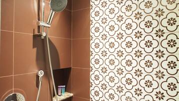 Un baño con baldosas marrones, una ducha con cabezal de ducha de mano y una pared con un diseño de azulejos florales.