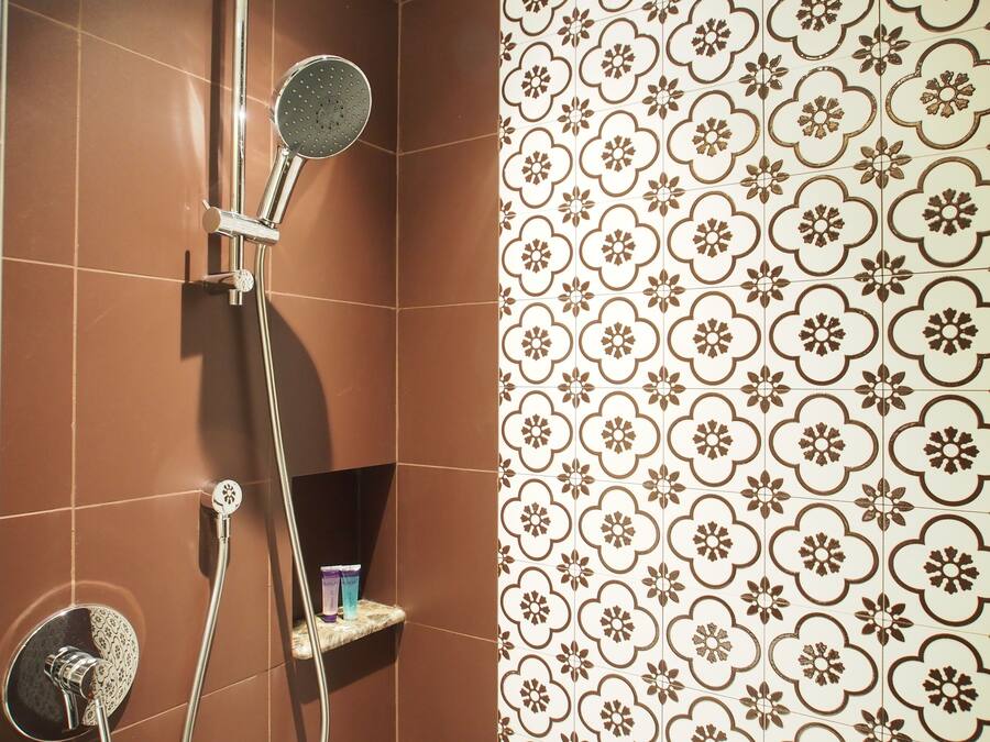 Un baño con baldosas marrones, una ducha con cabezal de ducha de mano y una pared con un diseño de azulejos florales.