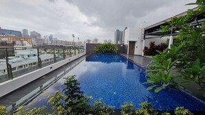 Une piscine sur le toit offrant une vue sur la ville, entourée de plantes et bordée d’une architecture moderne.