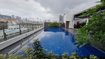 Una piscina en la azotea con vistas a la ciudad, rodeada de plantas y arquitectura moderna.