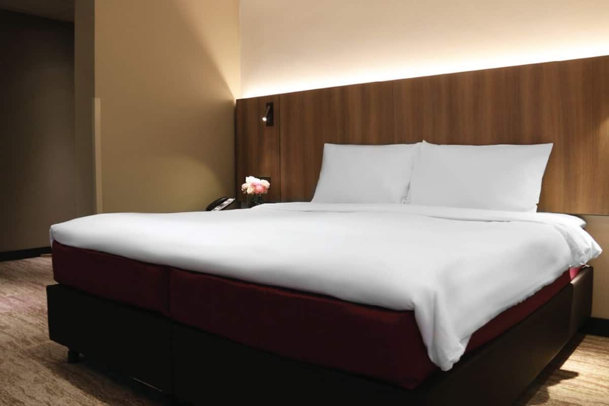 Une chambre d’hôtel avec un grand lit, une tête de lit en bois, une table de chevet avec un téléphone et un vase rempli de fleurs.