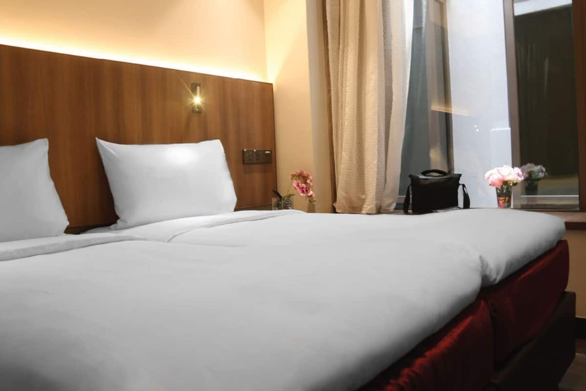 Une chambre d’hôtel avec un grand lit, une tête de lit en bois, une table de chevet avec une lampe et une fenêtre avec des rideaux.