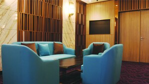 Une pièce avec un canapé bleu, deux fauteuils, une petite table, un téléviseur fixé au mur et un tapis à motifs.