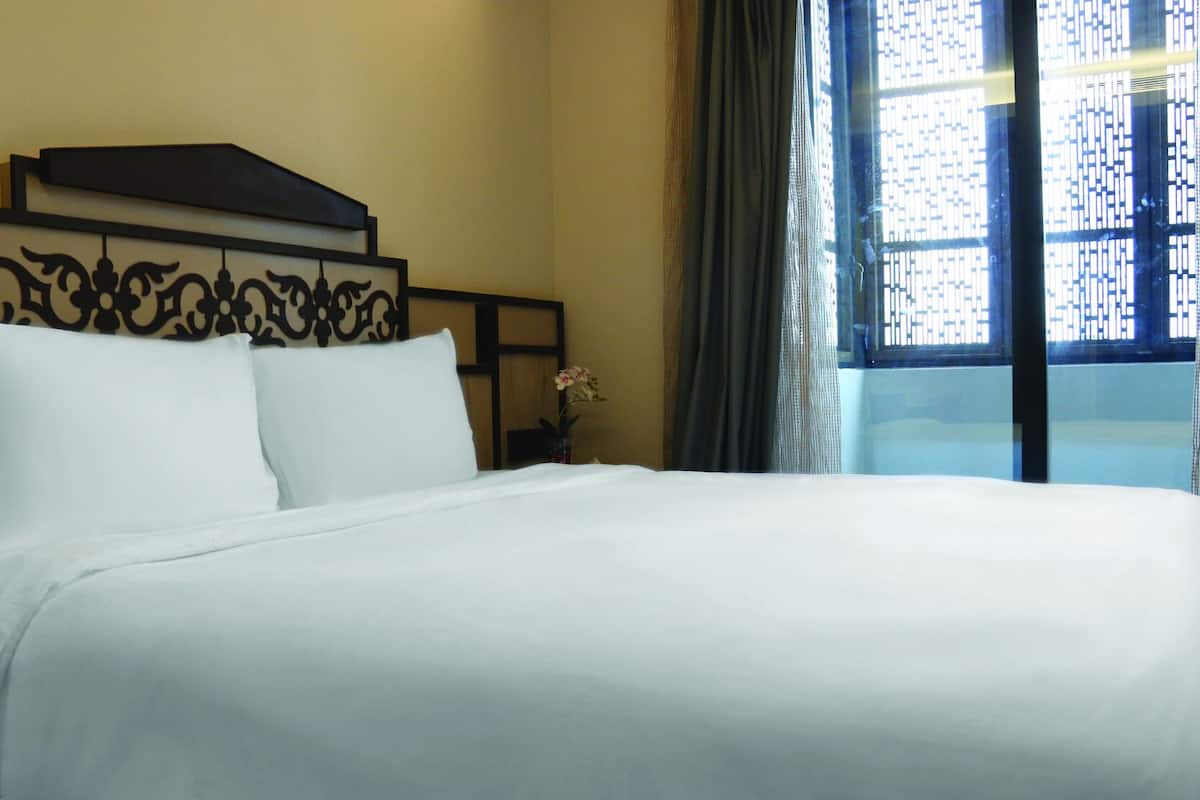 Un lit bien fait dans une chambre d’hôtel, avec une tête de lit, une fenêtre donnant sur un beau paysage et un vase rempli de fleurs sur la table de chevet.