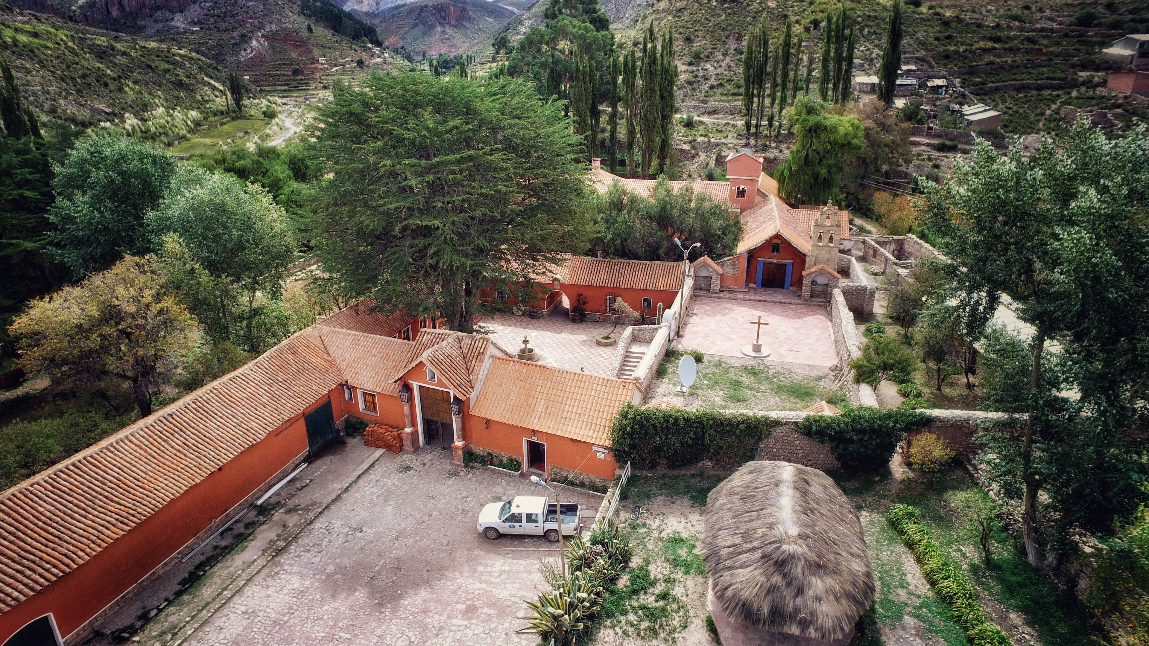 A rural village with terracotta-roofed buildings, a church, and a white pickup truck parked in front.