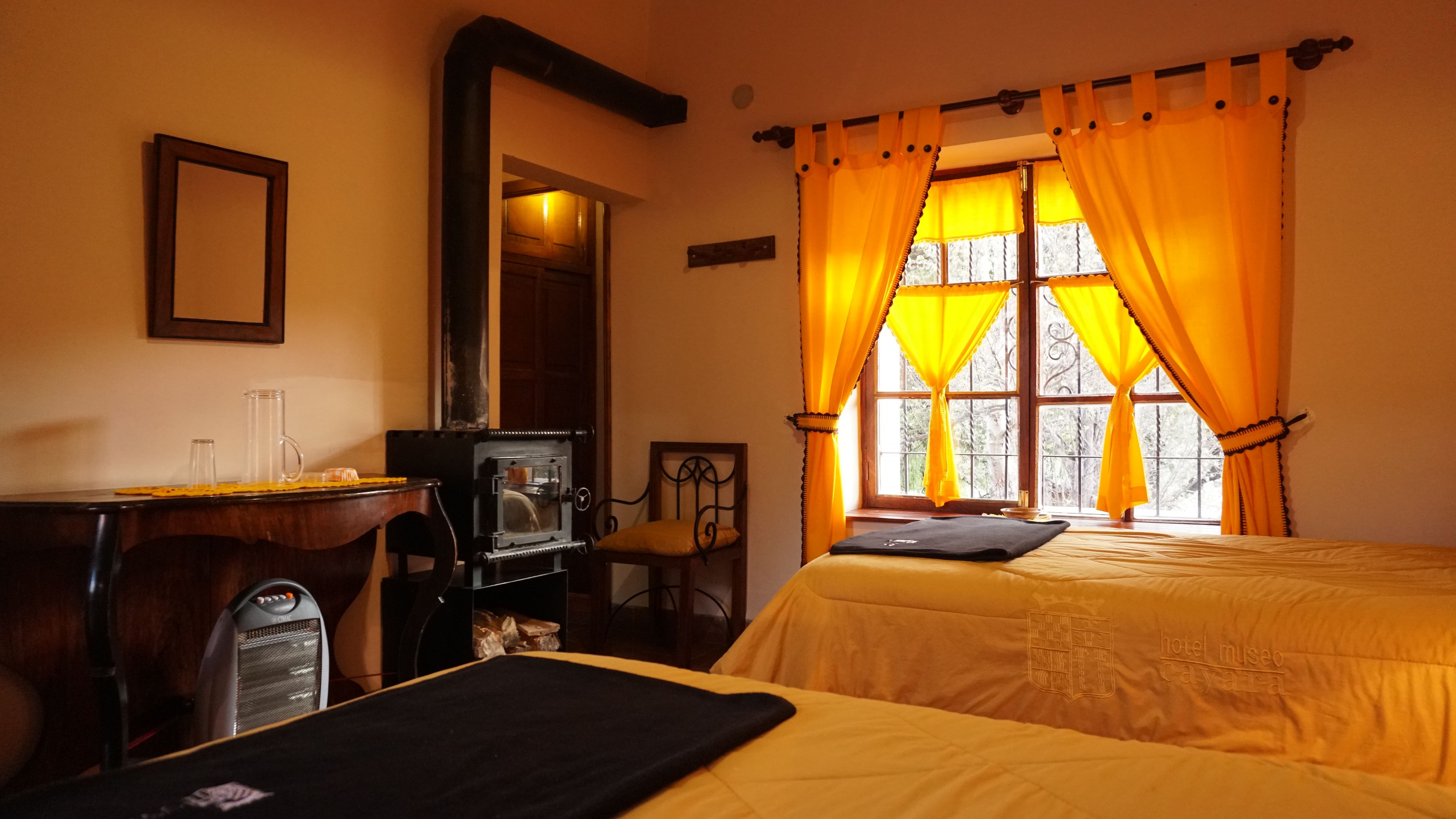 Habitación de hotel con dos camas, un escritorio con computadora, una silla y una ventana con cortinas.
