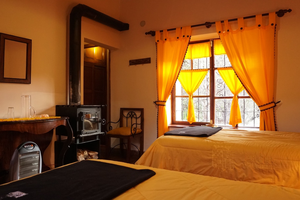 A hotel room with two beds, a desk with a computer, a chair, and a window with curtains.